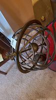 Side angle view of brass metal armillary sphere sculpture showing concentric rotating rings and base
