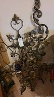 Two of the metal wall art pieces grouped against wall showing elaborate scroll and leaf designs in dark metallic tones with gold accents