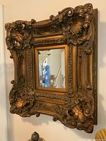 Full view of the ornate gold-tone framed beveled mirror hung on a wall.