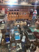 Display cabinet shelf with carved wooden streetcar, black woodie station wagon, and assorted model cars visible