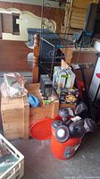 Photo of lot showing ten outdoor solar path lights with gray bases arranged on an orange bucket, wooden table holding two boxes of GELUVER Disk Lights, star-shaped lights, and other items.
