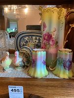 Porcelain pitcher with floral and gold design alongside three matching cups and turkey salt and pepper shakers on display.