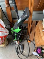 Full view of the pressure washer showing the green body, handle, black power cord, and attached spray wand with hose.