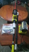 Hedge trimmer, battery, charger and instruction manual displayed on wood table