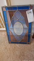 Full view of the rectangular stained glass panel with blue and clear glass designs and central oval mirror, showing metal framing and hanging hardware.
