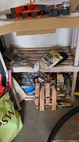 Shelf with wooden bar clamps, caulking gun, box of outlet kit, extension cords, and weather sealer.