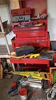 Red Taskforce tool chest with drawers containing various hand tools, toolboxes, and a yellow Stanley hand saw laid on and around it.