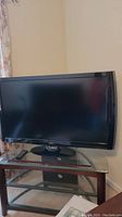 Front view of the Vizio TV and remote on a glass shelf with a wooden and metal stand