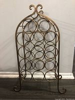 Front view of the metal wine bottle holder rack showing 14 circular slots for bottles and decorative scroll top design.