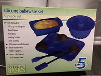 Box front showing set contents and features including 12-cup muffin pan, bundt pan, loaf pan, pastry brush and spatula, FDA approved silicone, heat resistant to 500°F/260°C, oven/microwave/freezer safe.