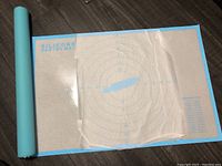 Photo of blue silicone pastry mat unrolled on a wooden floor, showing concentric circles and measurements.
