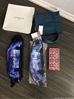 Overview of small gift set items including two fanny packs with 'Fancy Munroe' print, wallet, small blue tote, passport holder, and Liz Claiborne luggage box.