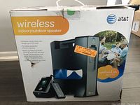 Front and side views of the original boxed packaging showing the AT&T wireless indoor/outdoor speaker system, highlighting key features such as 150 feet wireless range, 20 watt power, portability, and compatibility with Apple devices.