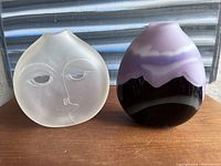 Two signed glass vases: one frosted satin glass vase shaped like a face and one purple European art glass vase with layered colors and matte finish.