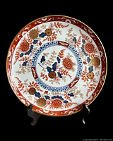 Imari porcelain plate with chrysanthemum flower design displayed on black stand, white background