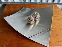 Triangular metal tray with two colorful spiked balls displayed on top, showing surface details and shape.