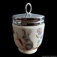 Front view of Royal Worcester double egg coddler showing rabbit with carrot and purple flower design on porcelain body and silver-toned metal lid with handle.