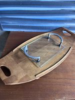 Large teak tray with carved handles and smaller glass tray with tubular metal handles placed on top.