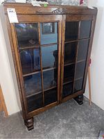 Front view of cabinet showing two glass-paned doors, carved crest, bun feet