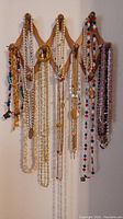 Front view of the wooden necklace holder with a variety of necklaces hanging including bead necklaces, faux pearls, gold colored chains, and shell necklaces.