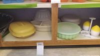 Plastic food storage containers including yellow and green lidded containers, round fluted containers, white plates, and egg holders with yellow tops on the shelf.