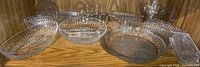Photo of assorted clear glass bowls, dishes, and trays showing ribbed designs and starburst patterns on some bases, arranged on a wooden shelf.