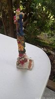 Full view of outdoor painted gnome statue on white table showing side profile with trees in background
