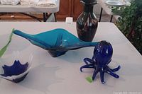 Photo showing all items on a white table: blue dish, dark vase, blue and white candle holder, blue octopus figurine.