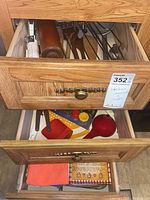 Two drawers open showing an assortment of kitchen gadgets and textiles including rolling pins, wooden spoons, ladle, hand mixer, slicer, and dish towels.