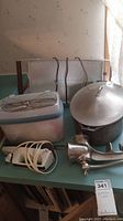 Lot contents: metal meat grinder with wooden handle, large pot with lid, electric hand mixer with cord and beaters, warming tray, plastic storage container with lid