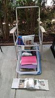 Metal frame chair, plastic bin with pink folder and materials, binder with photos on ground