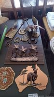 Wide view of metal wall art with birds, kangaroo plaque, brass scoops, and medallions on dark surface.