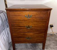 Front view of the wooden nightstand showing three drawers with metal handles.
