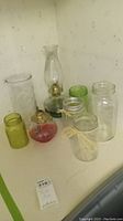 Lot contents showing three oil lamps and five ball jars of different sizes and colors arranged on a shelf.
