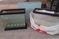 Two rectangular mirrored tealight holders with dark wood trim on top and bottom, one with six white tealights inside, situated on carpet next to a light blue Partylite box and a plastic bag.