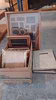 Various picture frames organized inside a box alongside photo albums placed on the floor