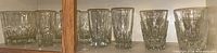 Shelf with clear glassware including faceted rocks glasses and smooth highball water glasses.