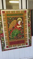 Full front view of handmade quilt with angel design hanging against a white wall.