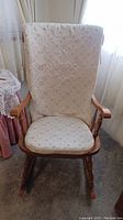 Front view of the rocking chair showing padded floral cushions on seat and backrest, wooden armrests, and rockers.