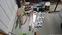 Tools including hand saws, levels, splitting maul, loppers, wedge, and nails displayed on porch floor