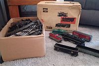 Multiple electric model train locomotives and cars displayed next to original AllState box with wear and tears.