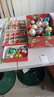 Wide view of three boxes filled with assorted vintage glass Christmas ornaments in various colors and shapes