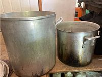 Two large aluminum pots without lids, showing size difference and handles.