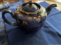Blue china tea pot with gold floral decorations on body, spout, handle, and lid.