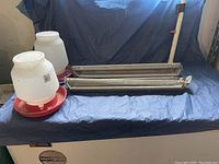 Photo of two plastic chicken waterers and two metal chicken feeders on a dark blue cloth.