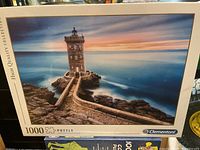 1000-piece lighthouse puzzle by Clementoni showing box front with image of lighthouse on rocky coast at sunset.