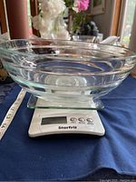 Clear glass bowl approximately 10 inches across placed on the white Starfrit digital kitchen scale on a dark blue cloth.