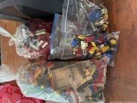 Four plastic bags of varying sizes filled with assorted original Lego bricks in multiple colors and shapes including some space-themed elements.