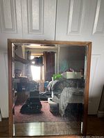 Photo showing front of large rectangular mirror reflecting room interior with curtain and furniture