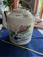 Front view showing the large ceramic teapot with hand-painted floral and bird designs and bamboo handle.